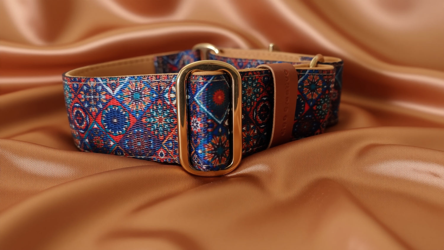 A colorful patterned dog collar with a gold buckle.