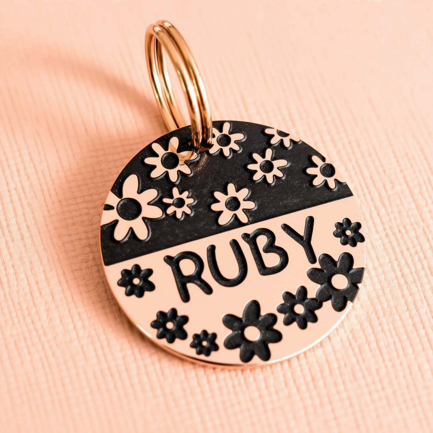 A round metal pet tag with a floral design and the name "Ruby" printed on it.
