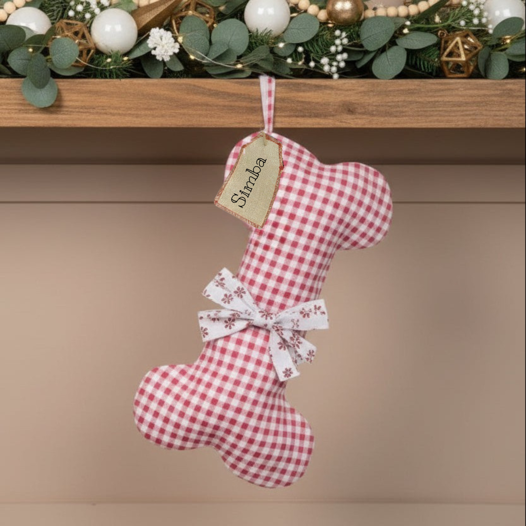 Red and white checkered Christmas dog stocking with a bow and 'personalised' tag hanging on a wooden mantel.